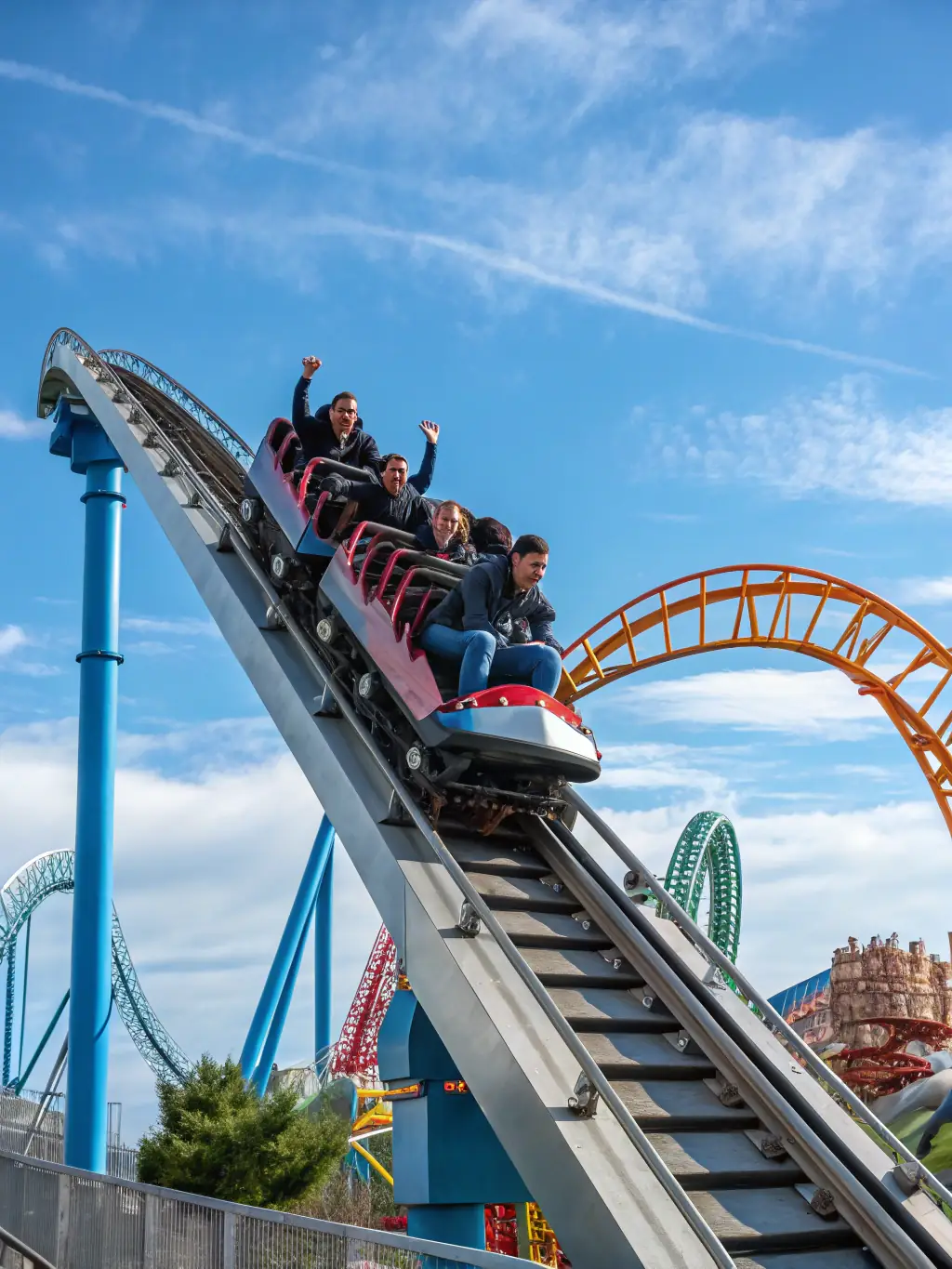 A high-angle, slightly blurred action shot of the Hyperion roller coaster at Energylandia, focusing on the steep drop and the thrill on riders' faces. The sky is clear and blue in the background.